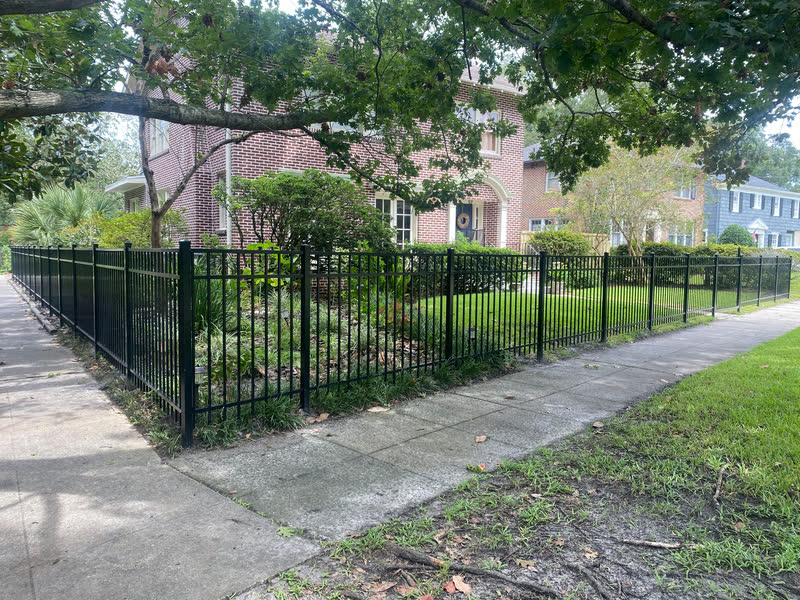 Black aluminum fence with puppy panel pickets along a brick home sidewalk garden