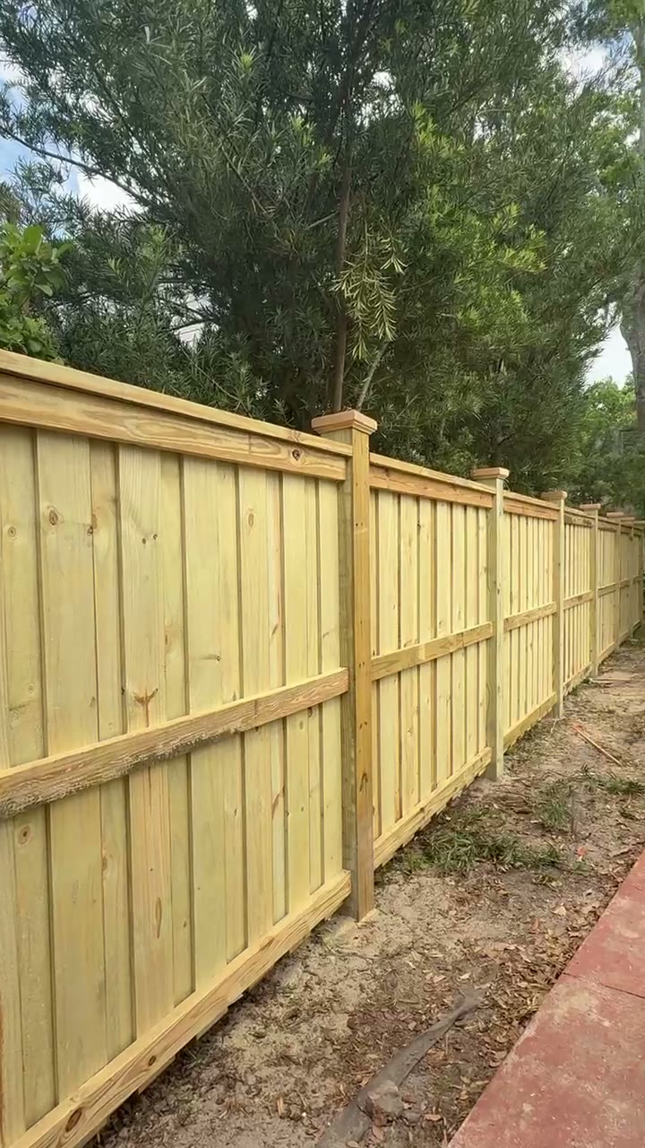 Tall board on board privacy fence with decorative post caps beside a shaded yard
