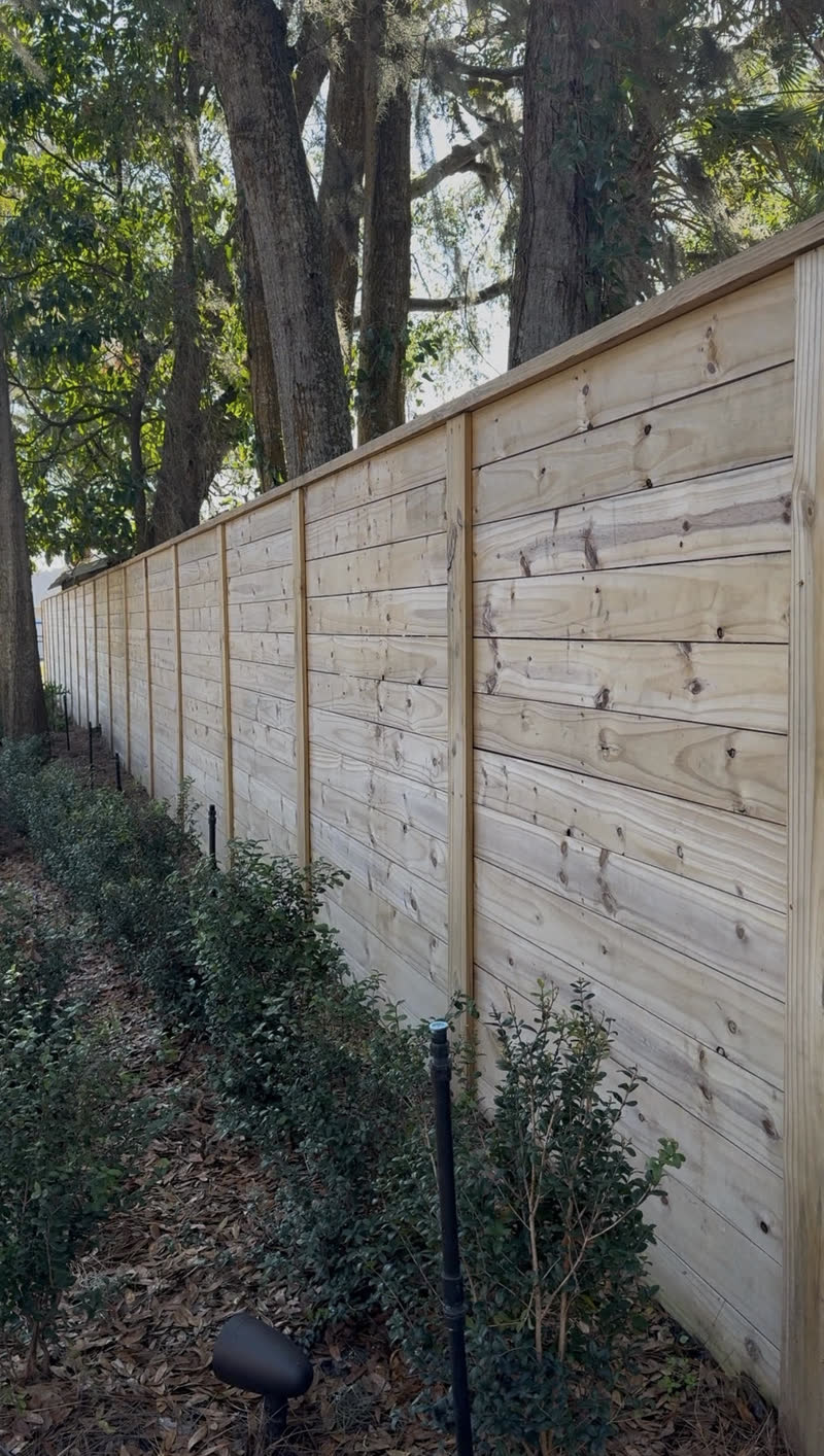 Tall horizontal board privacy fence with clean level lines along a hedge row