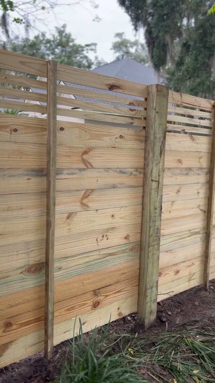 Horizontal slat privacy fence with reveal gaps and a matching gate behind a hedge
