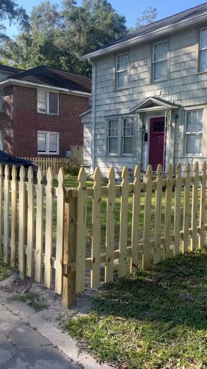 New open picket fence with pointed pickets in front of a home with a red door