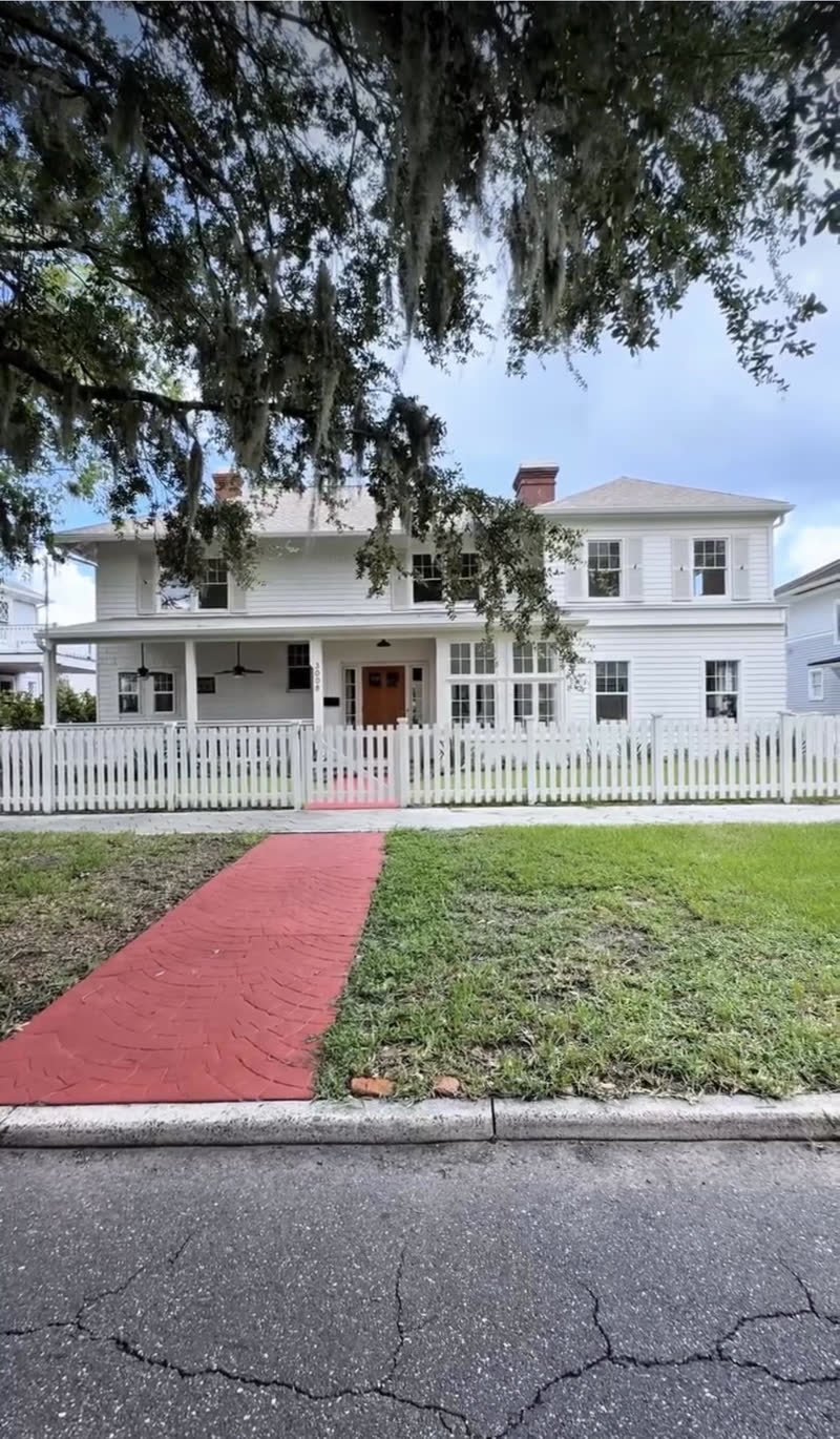 White open picket fence fronting a historic two story home with a red brick walkway