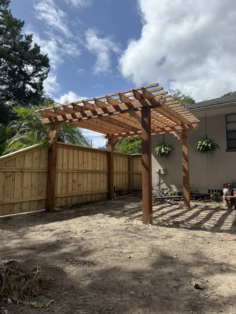 Finished cedar pergola beside a board on board fence under a blue Florida sky