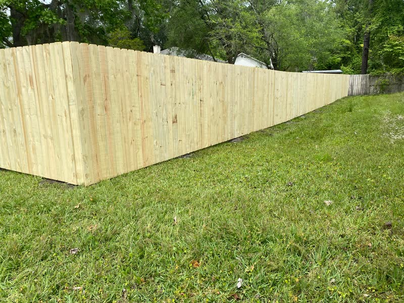 Fresh stockade privacy fence stepping down a grassy hillside in bright sun