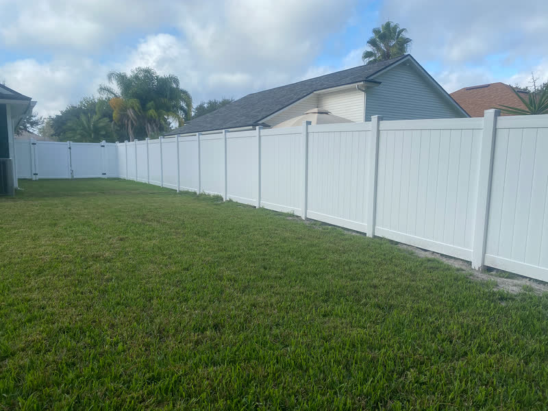 White vinyl privacy fence enclosing a green backyard under palm trees